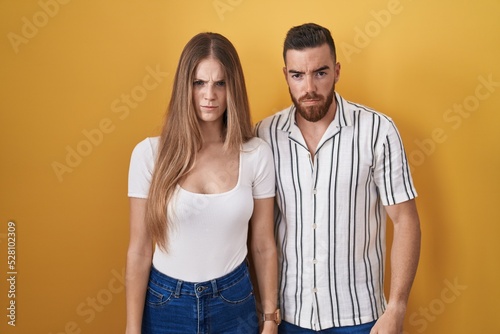 Young couple standing over yellow background skeptic and nervous, frowning upset because of problem. negative person.