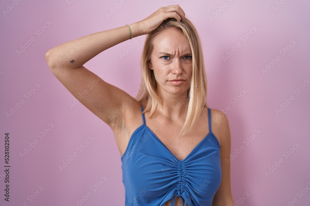 Young caucasian woman standing over pink background confuse and wondering about question. uncertain with doubt, thinking with hand on head. pensive concept.
