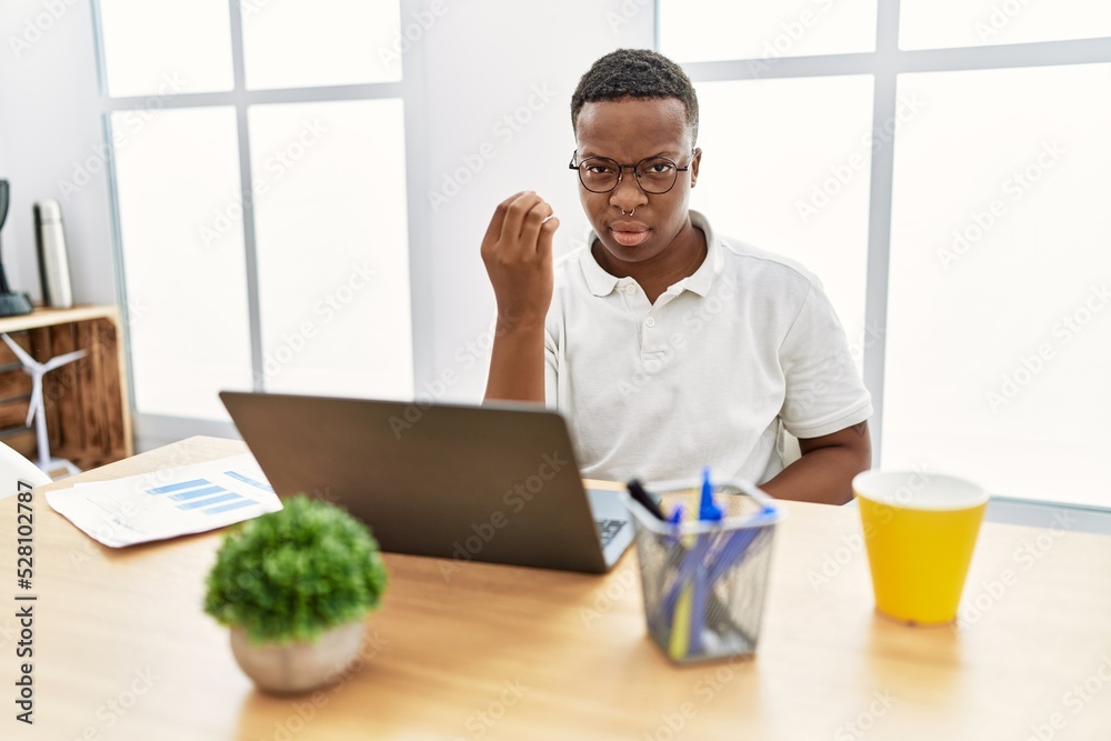 Young african man working at the office using computer laptop doing italian gesture with hand and fingers confident expression