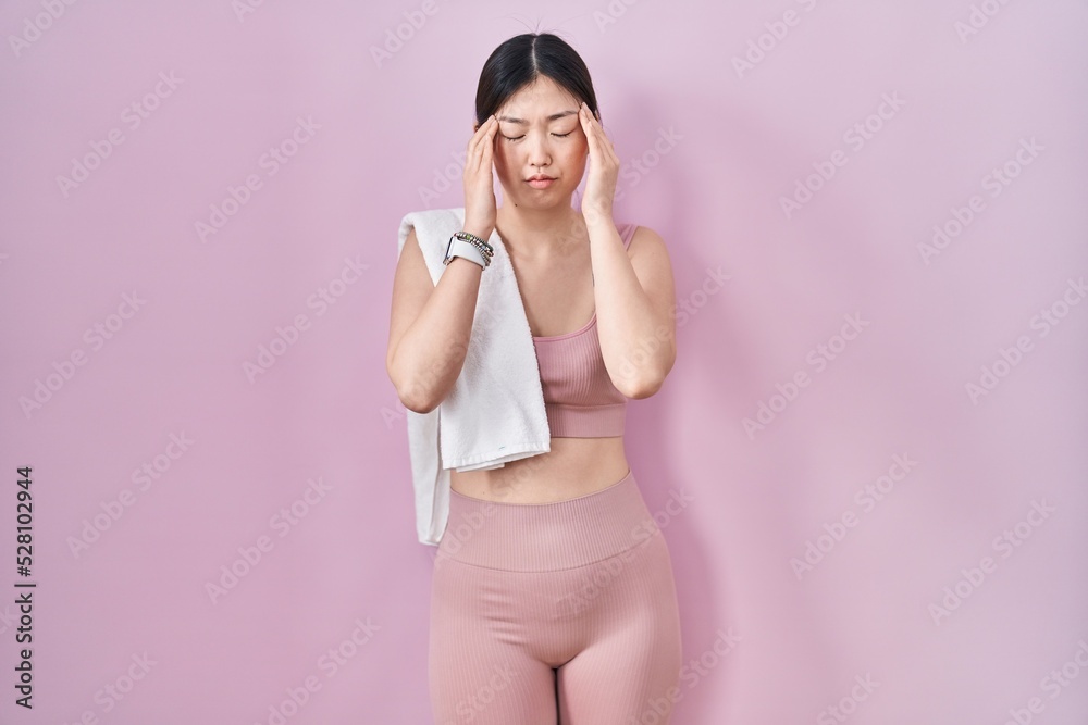 Chinese young woman wearing sportswear and towel with hand on head, headache because stress. suffering migraine.