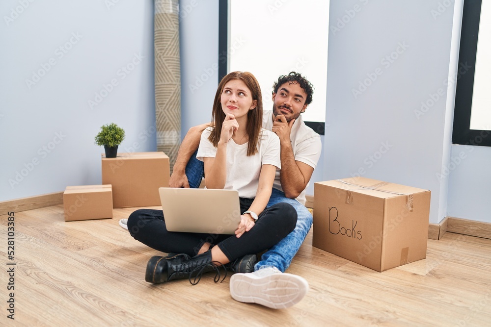 Young couple using laptop at new home with hand on chin thinking about question, pensive expression. smiling and thoughtful face. doubt concept. Young couple using laptop at new home with hand on chin thinking about question, pensive expression. smiling and thoughtful face. doubt concept.