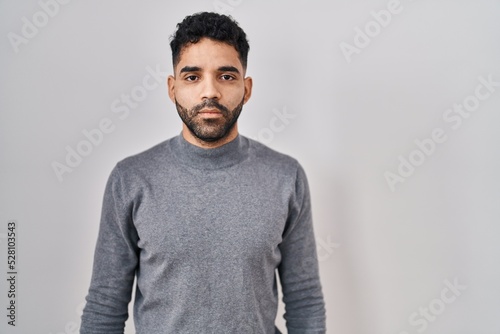 Hispanic man with beard standing over white background relaxed with serious expression on face. simple and natural looking at the camera. © Krakenimages.com