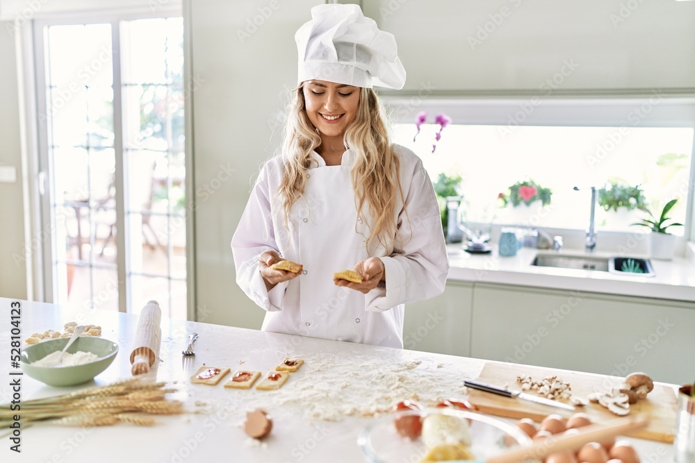 Young woman wearing cook uniform holding homemade pasta at kitchen Young woman wearing cook uniform holding homemade pasta at kitchen