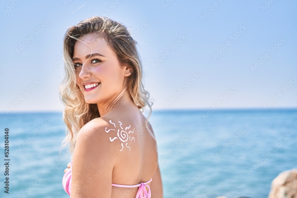 Young blonde girl with sunscreen sun draw on her back standing at the beach.