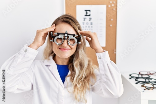 Young beautiful optician woman wearing optometry glasses at the clinic suffering from headache desperate and stressed because pain and migraine. hands on head.