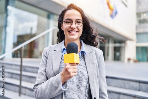 Young hispanic woman reporter working using microphone at street photo