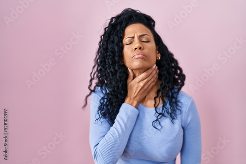 Middle age hispanic woman standing over pink background touching painful neck  sore throat for flu  clod and infection
