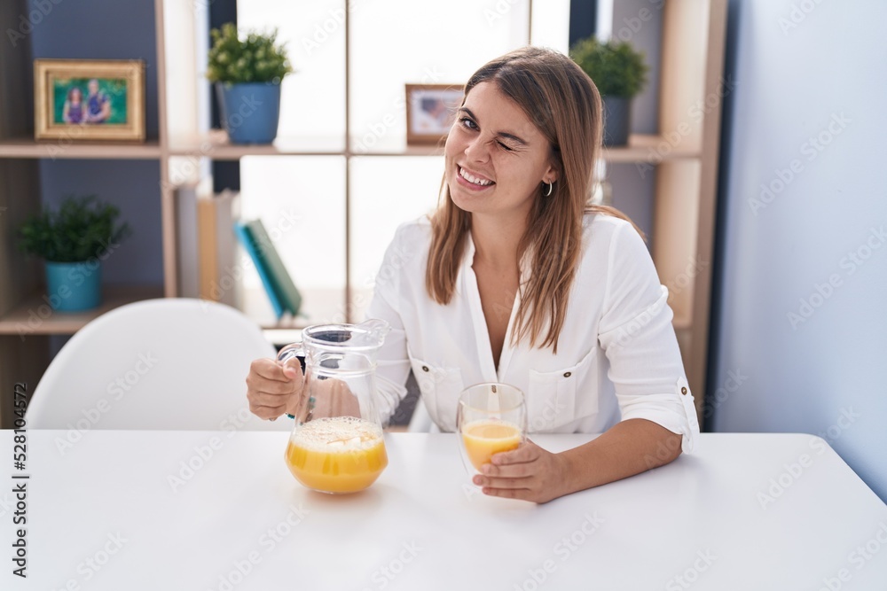 Young hispanic woman drinking glass of orange juice winking looking at the camera with sexy expression, cheerful and happy face. Young hispanic woman drinking glass of orange juice winking looking at the camera with sexy expression, cheerful and happy face.
