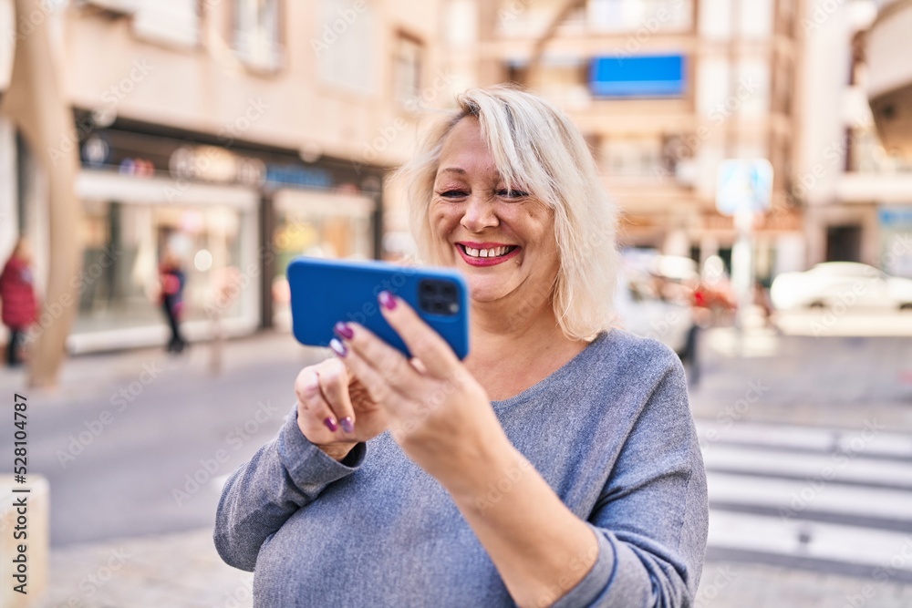 Middle age blonde woman smiling confident using smartphone at street