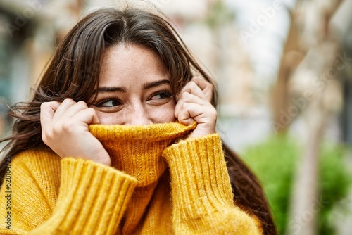 Young beautiful brunette woman wearing turtleneck sweater doing funny gesture covering face with sweater