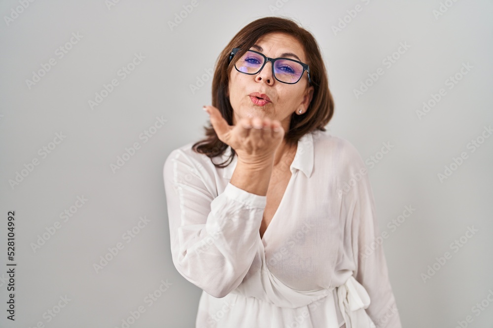 Middle age hispanic woman standing over isolated background looking at the camera blowing a kiss with hand on air being lovely and sexy. love expression. Middle age hispanic woman standing over isolated background looking at the camera blowing a kiss with hand on air being lovely and sexy. love expression.