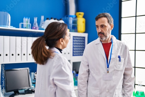 Middle age man and woman scientists standing together at laboratory
