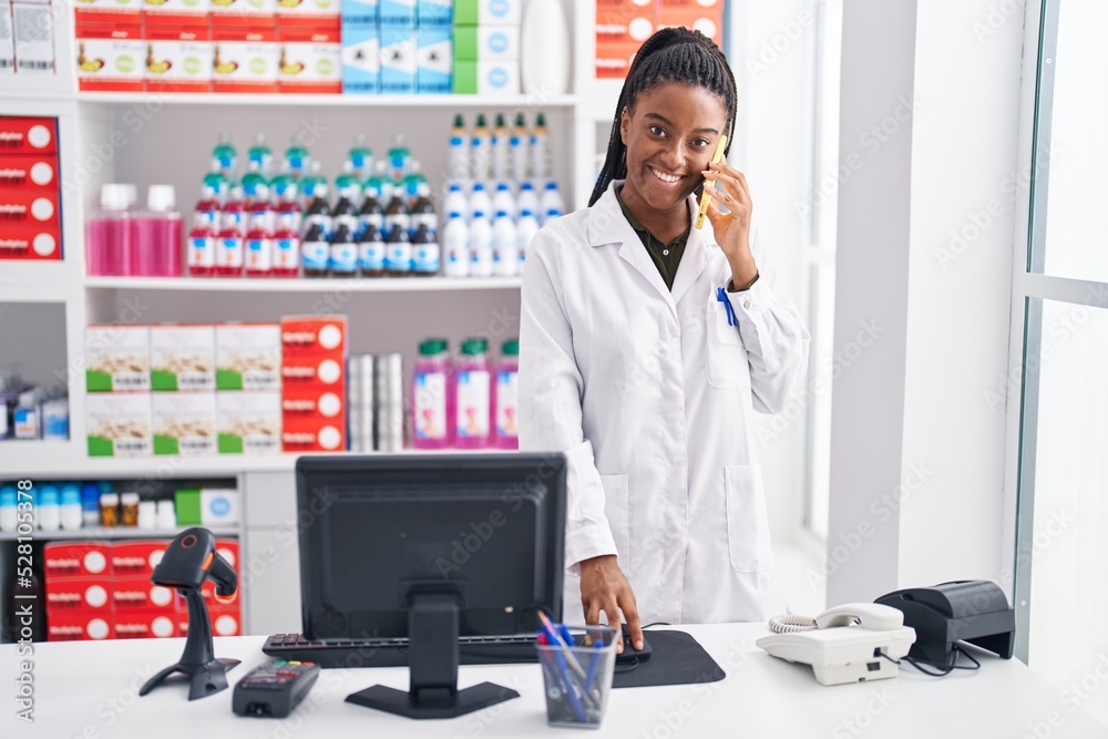 African american woman pharmacist talking on smartphone using computer at pharmacy African american woman pharmacist talking on smartphone using computer at pharmacy
