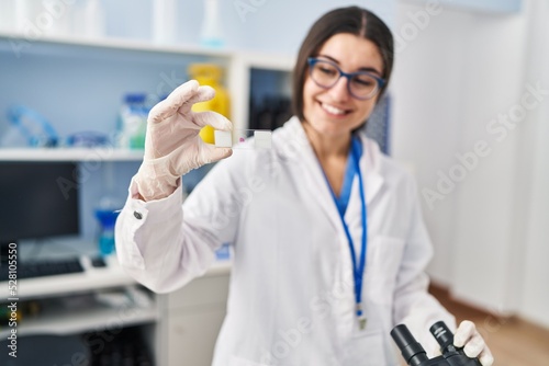 Fototapeta Naklejka Na Ścianę i Meble -  Young hispanic woman wearing scientist uniform using microscope at laboratory