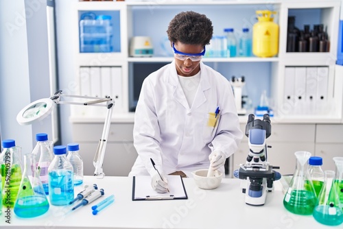 African american woman wearing scientist uniform write on clipboard working at laboratory