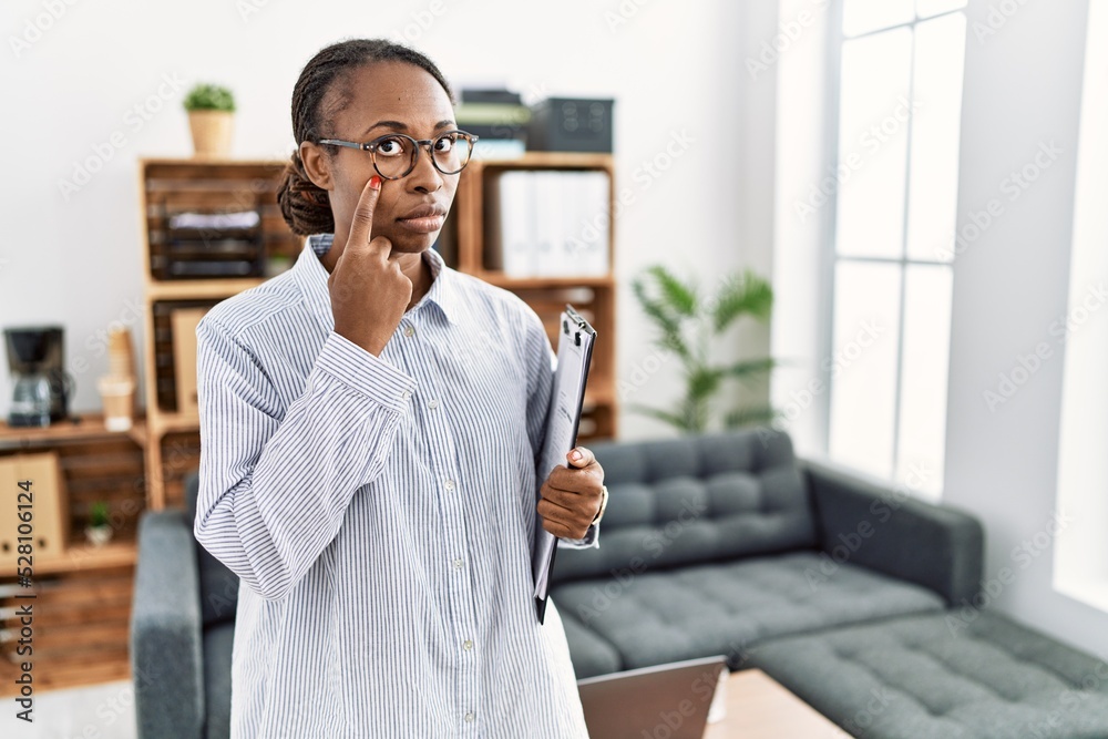Fototapeta premium African woman working at psychology clinic pointing to the eye watching you gesture, suspicious expression