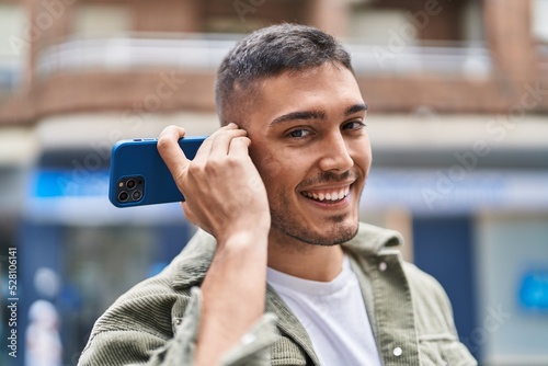 Young hispanic man smiling confident listening audio message by the smartphone at street
