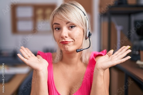 Young caucasian woman wearing call center agent headset clueless and confused expression with arms and hands raised. doubt concept.