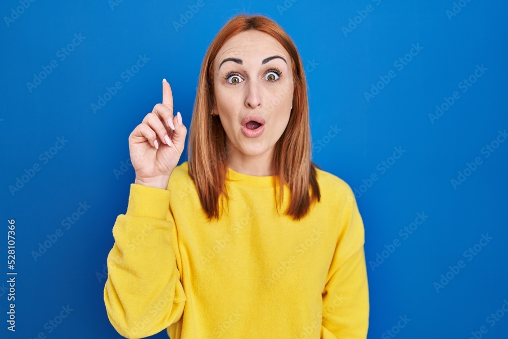 Young woman standing over blue background pointing finger up with successful idea. exited and happy. number one. Young woman standing over blue background pointing finger up with successful idea. exited and happy. number one.