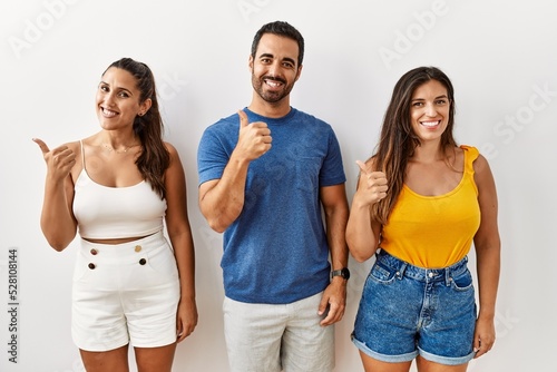 Group of young hispanic people standing over isolated background doing happy thumbs up gesture with hand. approving expression looking at the camera showing success.