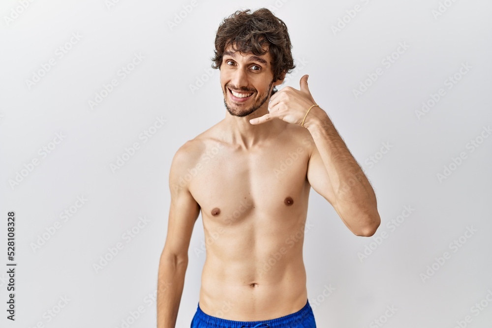 Young hispanic man standing shirtless over isolated, background smiling doing phone gesture with hand and fingers like talking on the telephone. communicating concepts.