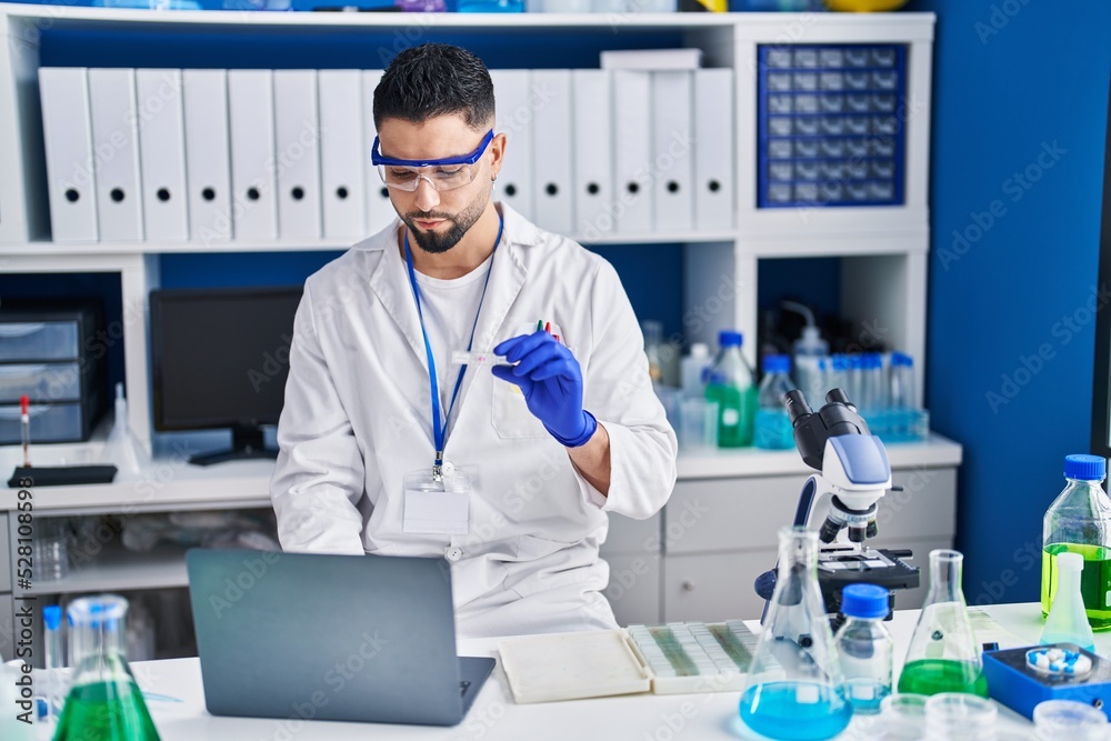 Young arab man scientist using laptop holding sample at laboratory Young arab man scientist using laptop holding sample at laboratory