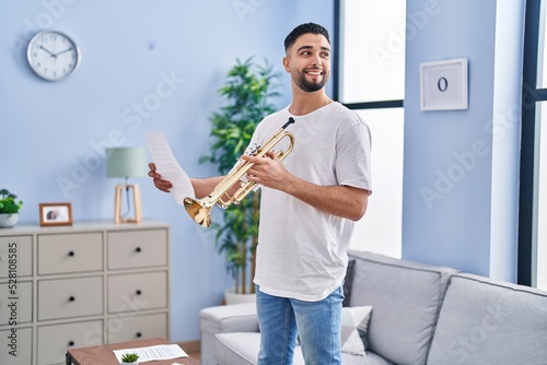 Canvas Print Young arab man musician holding trumpet and music sheet at home