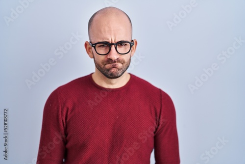 Young bald man with beard standing over white background wearing glasses skeptic and nervous, frowning upset because of problem. negative person. © Krakenimages.com
