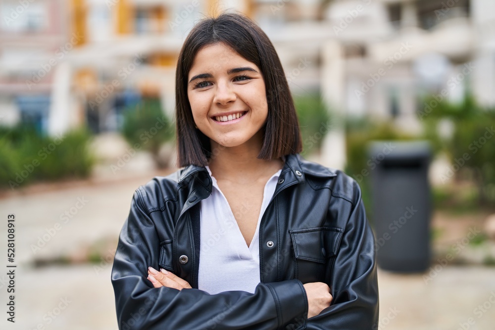 Young beautiful hispanic woman standing with arms crossed gesture at park