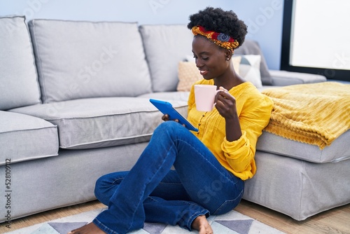 Young african american woman drinking coffee and using touchpad at home