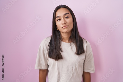 Young hispanic woman standing over pink background looking sleepy and tired, exhausted for fatigue and hangover, lazy eyes in the morning.