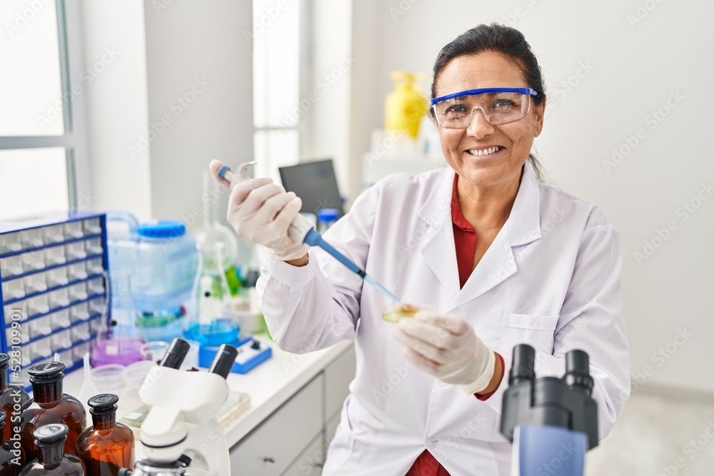 Middle age hispanic woman wearing scientist uniform using pipette at laboratory