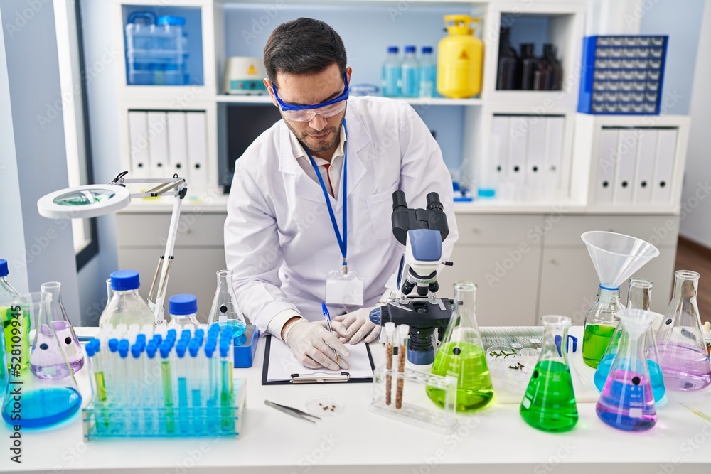 Young hispanic man scientist writing on document at laboratory Young hispanic man scientist writing on document at laboratory