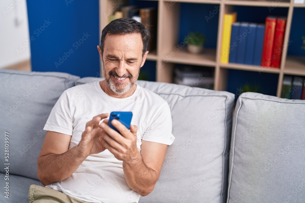Middle age man using smartphone sitting on sofa at home Middle age man using smartphone sitting on sofa at home