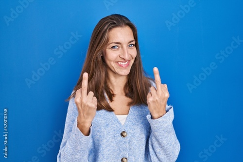 Young woman standing over blue background showing middle finger doing fuck you bad expression, provocation and rude attitude. screaming excited