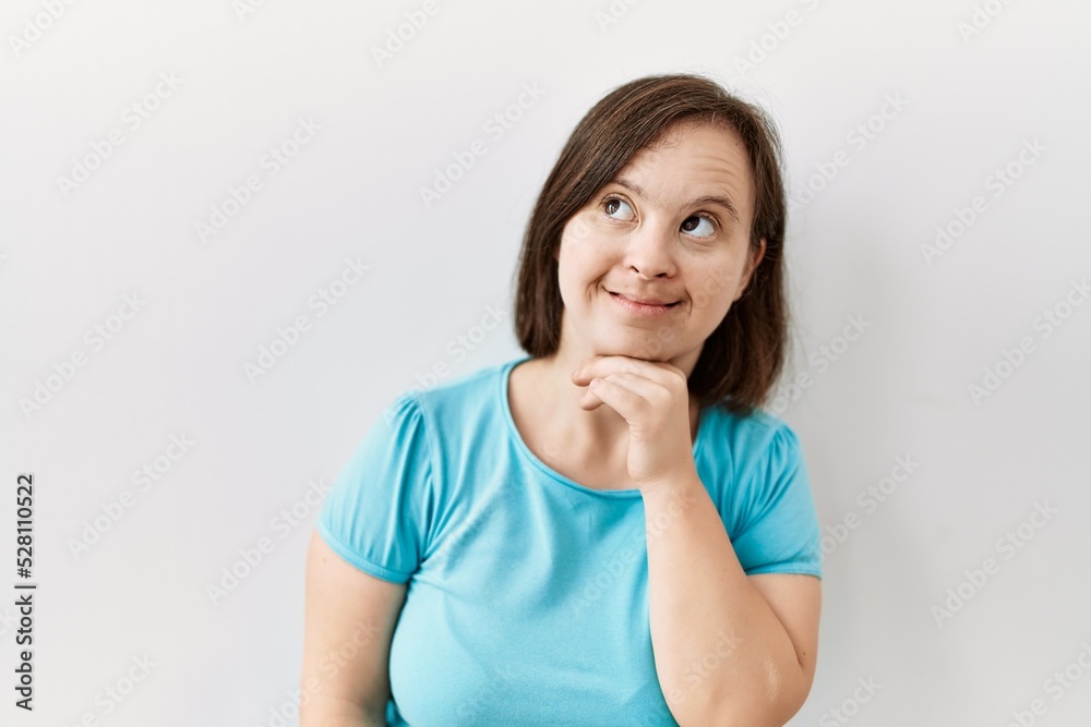 Young down syndrome woman standing over isolated background looking confident at the camera with smile with crossed arms and hand raised on chin. thinking positive. Young down syndrome woman standing over isolated background looking confident at the camera with smile with crossed arms and hand raised on chin. thinking positive.