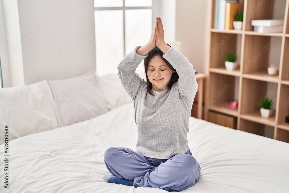 Young woman with down syndrome doing yoga exercise sitting on bed at bedroom Young woman with down syndrome doing yoga exercise sitting on bed at bedroom