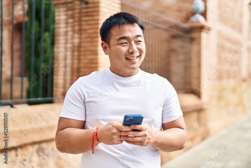 Young chinese man smiling confident using smartphone at street