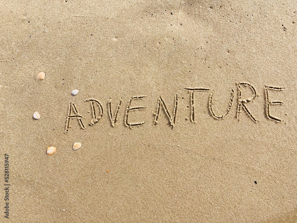 Fototapeta premium on the beach is carved with letters in the smooth sand the writing adventure