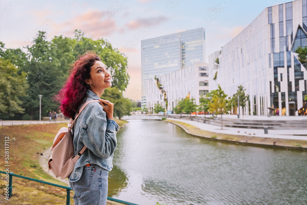 Happy tourist woman with backpack visiting Konigsallee water channel and admiring great modern architecture buildings in Dusseldorf, Germany Happy tourist woman with backpack visiting Konigsallee water channel and admiring great modern architecture buildings in Dusseldorf, Germany