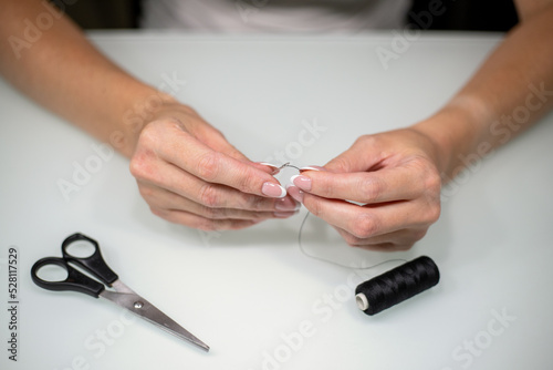 Woman threading sewing needle at table, closeup.
