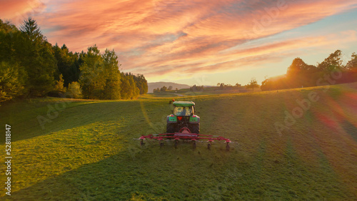 Foto AERIAL: Rear view of tractor turning mowed hay with hay tedder at autumn sunset