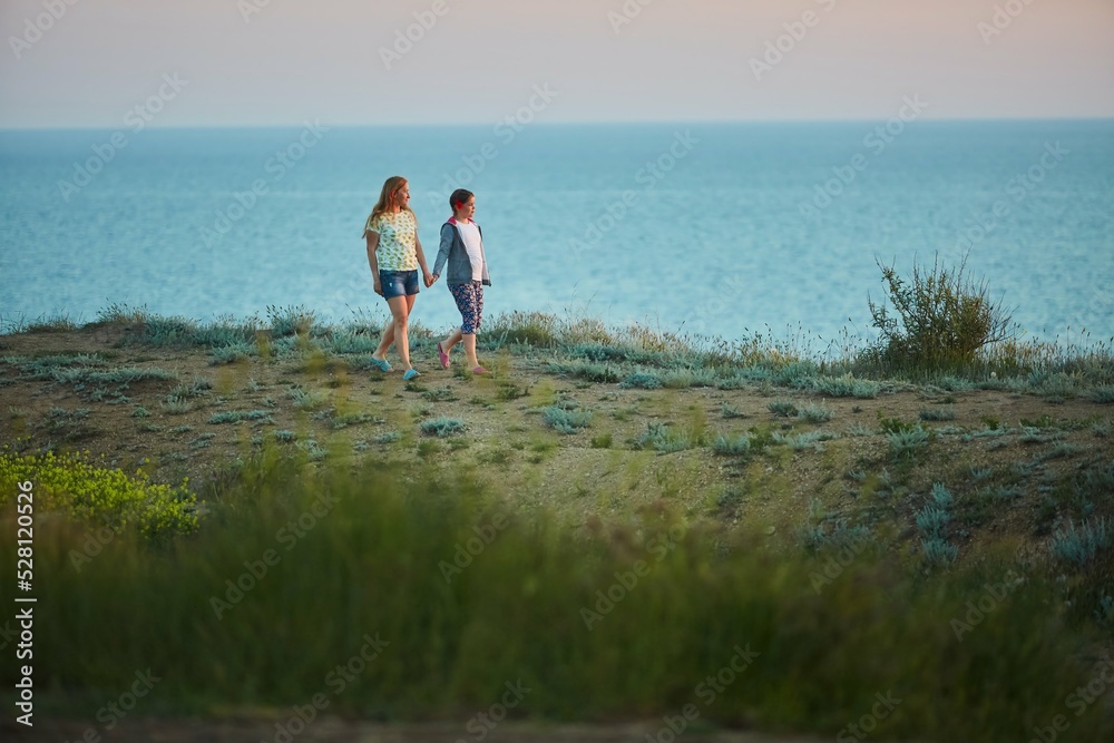 Mom and daughter are walking at sunset on the high seashore.