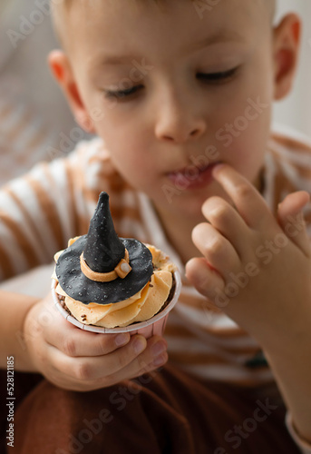 A little boy sits on the windowsill and eats a cupcake in the form of a witch's hat. Halloween concept