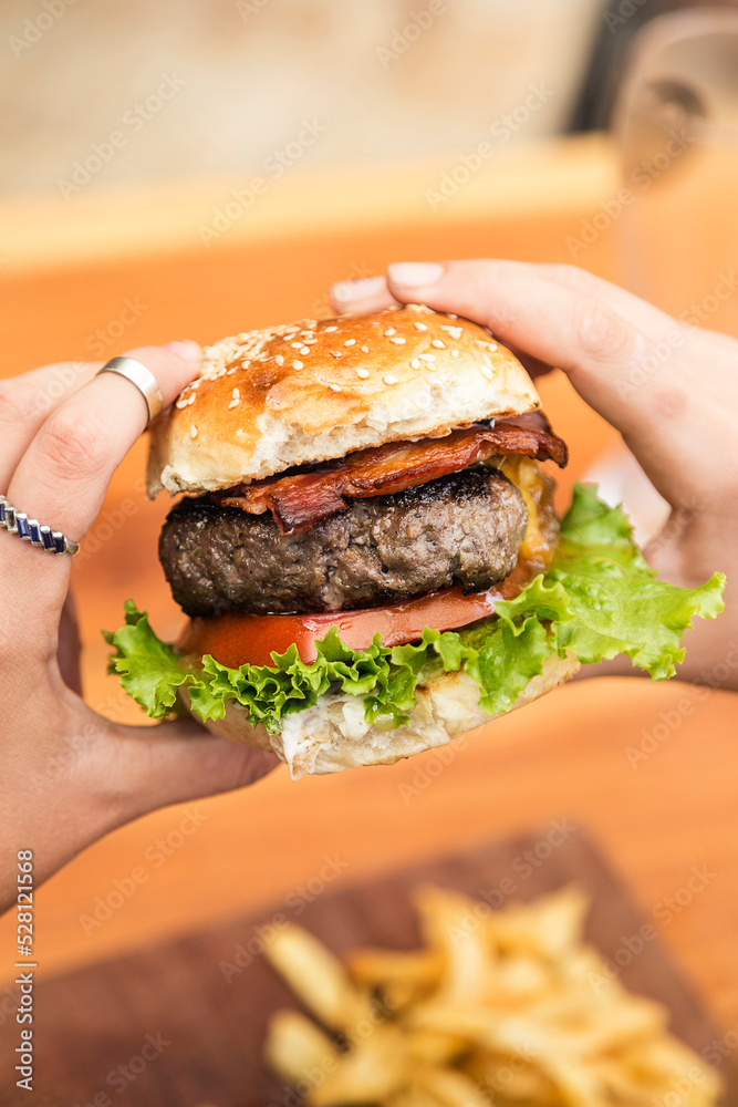 Hands holding a burger, on a restaurant table. Delicious and nutritious food. Hands holding a burger, on a restaurant table. Delicious and nutritious food.