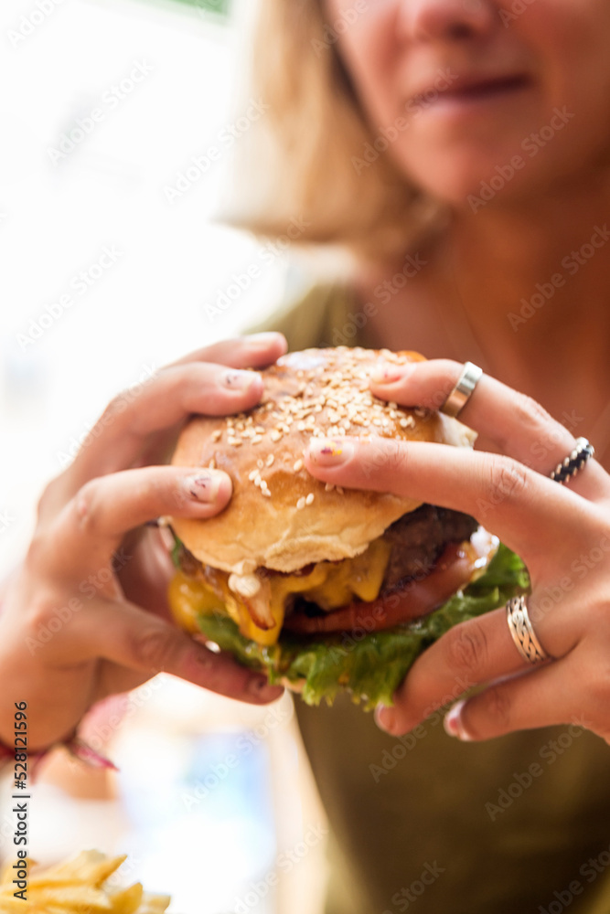 Hands holding a burger, on a restaurant table. Delicious and nutritious food. Hands holding a burger, on a restaurant table. Delicious and nutritious food.