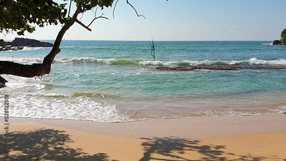 The Indian Ocean is seen from the betfred trees. Beautiful shiny turquoise waves wash over the yellow sand. High quality FullHD footage