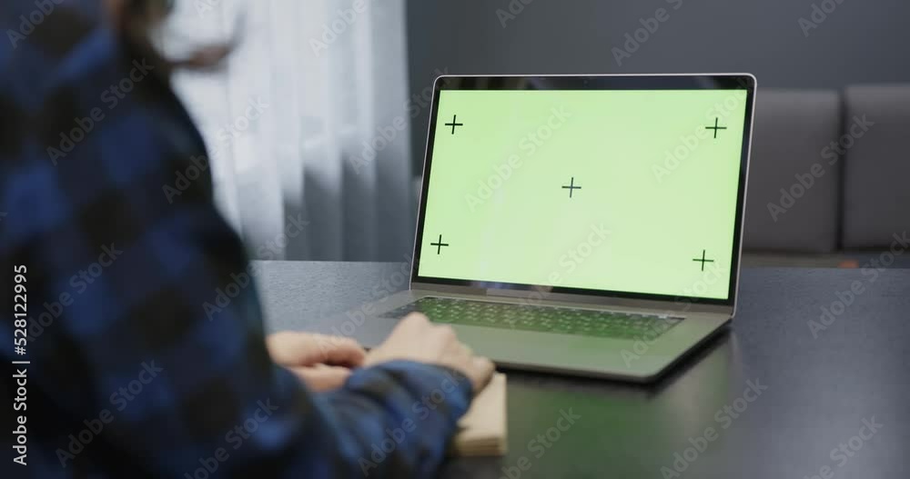 A laptop with a green screen is on the table, in front of the girl. A laptop with a green screen is on the table, in front of the girl.