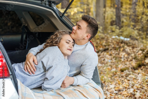 Boy and girl are hugging in trunk of car. Autumn forest. Couple in love. Romantic date.