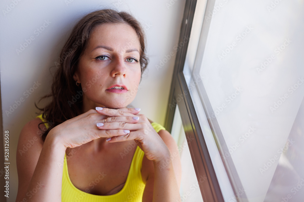 Young woman in yellow sportswear posing in sports club hall at window indoors. Sporty fit girl portrait. Smart elegant woman sitting on windowsill thoughtful. Top and leggings suit. Woman alone Young woman in yellow sportswear posing in sports club hall at window indoors. Sporty fit girl portrait. Smart elegant woman sitting on windowsill thoughtful. Top and leggings suit. Woman alone